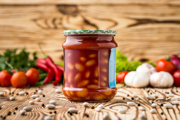 Composition of pickled beans with tomato in jar and ingredients on wooden background