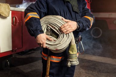 İtfaiyeci (itfaiye) yakınındaki bir firetruck haddelenmiş yangın hortumu ile eylem. Acil durum Emanet. Koruma, tehlikeden kurtarmak.