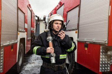 İtfaiyeci (itfaiye) eylem daimi bir firetruck yakınındaki. Acil durum Emanet. Koruma, tehlikeden kurtarmak.