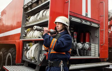 İtfaiyeci (itfaiye) eylem daimi bir firetruck yakınındaki. Acil durum Emanet. Koruma, tehlikeden kurtarmak.