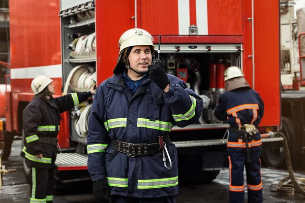 Strażak (strażaków) w akcji stojący w pobliżu wóz strażacki. Awaryjnych bezpieczeństwa. Ochrony, ratunek przed niebezpieczeństwem. — Zdjęcie stockowe