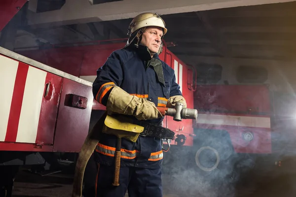 Brandweerman (brandweerman) in actie staande in de buurt van een brandweerwagen. De veiligheid van de noodsituatie. Bescherming, redding van gevaar. — Stockfoto