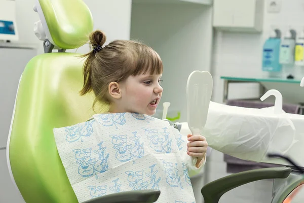 Kid girl in dentist\'s chair looks in the mirror. Dental problem.