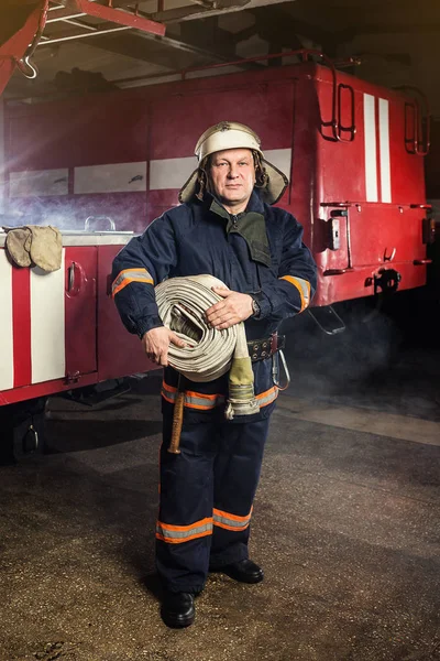 Brandweerman (brandweerman) in actie staande in de buurt van een brandweerwagen. De veiligheid van de noodsituatie. Bescherming, redding van gevaar. — Stockfoto