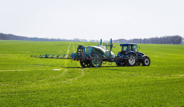 Tractor spraying insecticide to the green field, agricultural natural seasonal spring background