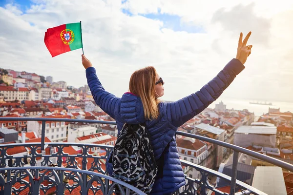 Nuori nainen turisti nauttimassa kauniista kaupunkimaisemasta vanhassakaupungissa pitäen Portugalin lippua käsissä aurinkoisena päivänä Lissabonissa — kuvapankkivalokuva