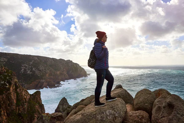 Young woman tourist at Cape Cabo da Roca standing on the rocky edge of the cliff. The waves of the ocean break on the rocks at the bottom of the cliff Royalty Free Stock Images