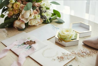 Ayakkabı, buket, yüzük ve davetiye kartları gibi düğün aksesuarları masanın üzerinde.