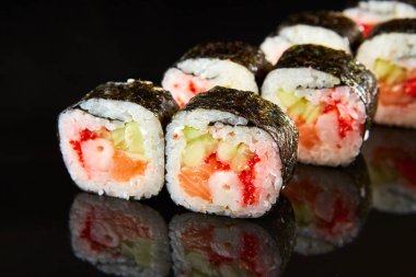 Geleneksel suşi rulosu, somon, krem peynir, karides ve siyah taş üzerinde salatalık. Japon yemeği.