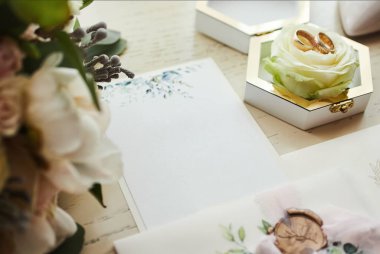 Ayakkabı, buket, yüzük ve davetiye kartları gibi düğün aksesuarları masanın üzerinde.