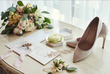 Ayakkabı, buket, yüzük ve davetiye kartları gibi düğün aksesuarları masanın üzerinde.
