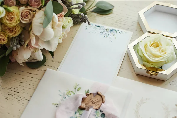 Ayakkabı, buket, yüzük ve davetiye kartları gibi düğün aksesuarları masanın üzerinde.