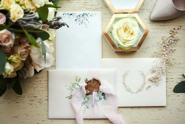 Ayakkabı, buket, yüzük ve davetiye kartları gibi düğün aksesuarları masanın üzerinde.