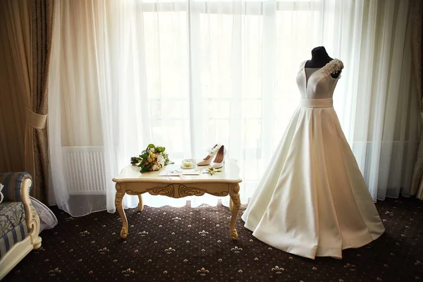 beautiful wedding dress hanging in the room, woman getting ready before  ceremony