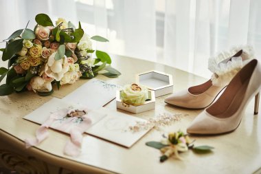 Ayakkabı, buket, yüzük ve davetiye kartları gibi düğün aksesuarları masanın üzerinde.