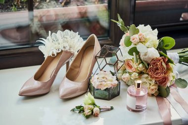 Ayakkabı, buket, yüzük ve parfüm gibi düğün aksesuarları bir masanın üzerinde bulunur.