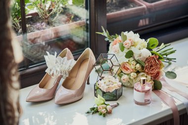 Ayakkabı, buket, yüzük ve parfüm gibi düğün aksesuarları bir masanın üzerinde bulunur.