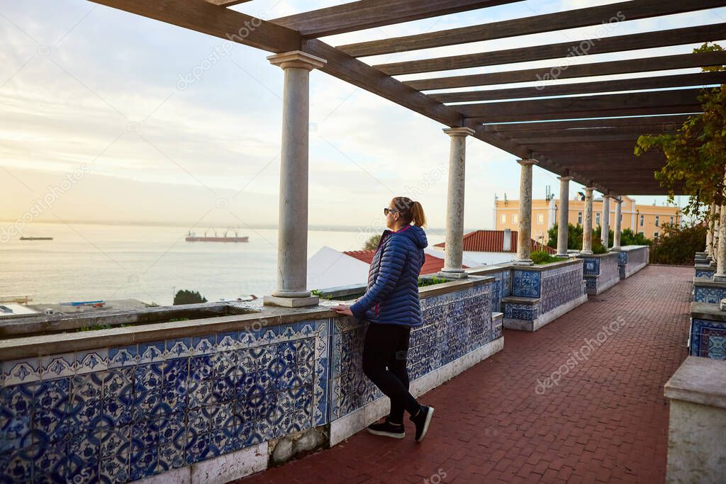Beautiful women tourist looks at the red roofs of Lisbon Portugal from the viewpoint Miradouro de Santa Luzia 