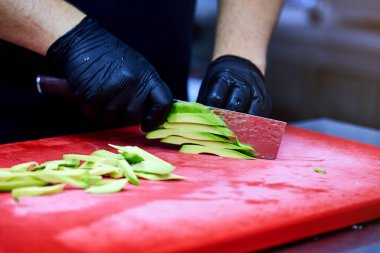 Kesme tahtasındaki kesilmiş avokado dilimlerini soyan eller.