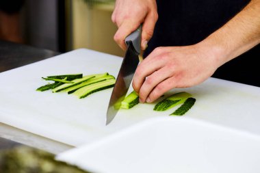 Kesme tahtasındaki salatalık dilimlerini soyan eller. Sebzeler salata için hazır. Lezzetli diyet vejetaryen yemekleri