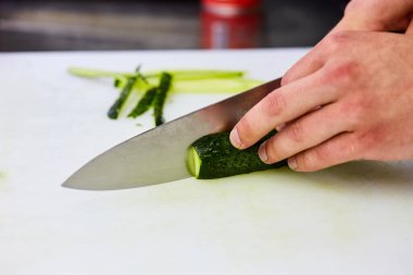 Kesme tahtasındaki salatalık dilimlerini soyan eller. Sebzeler salata için hazır. Lezzetli diyet vejetaryen yemekleri