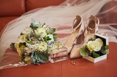 Bir sandalyede ayakkabı, buket, yüzük ve parfüm gibi düğün aksesuarları.