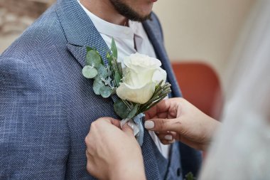 Gelin, damat yaka çiçeğini düğün hazırlıklarında ceketinde düzeltiyor.
