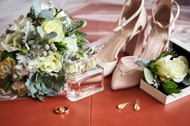 Bir sandalyede ayakkabı, buket, yüzük ve parfüm gibi düğün aksesuarları.