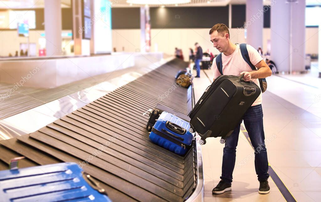 A male European traveler (passenger) picks up his luggage from the  baggage claim tape upon arrival (departure) at the Havalimani International Airport in Istanbul (IST Airport)
