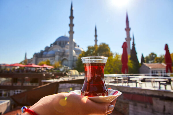 Кубок (броня) традиционного турецкого чая в руке на фоне мечети в Стамбуле

