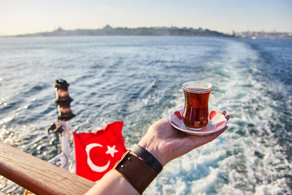 A cup (armud) of traditional Turkish tea  in hand against the background of the cityscape of Istanbul and the Sea of Marmar