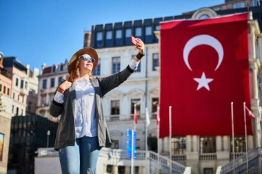 Çekici genç kadın turist, İstanbul 'daki Beyoğlu Belediye Binası' nda Türk bayrağının arka planında selfie çekiyor