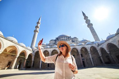 Şapkalı, poz veren ve poz veren mutlu çekici kadın turist, İstanbul, Türkiye 'deki Süleyman Camii' nin avlusunda fotoğraf çekiyor. Din ve seyahat kavramı.