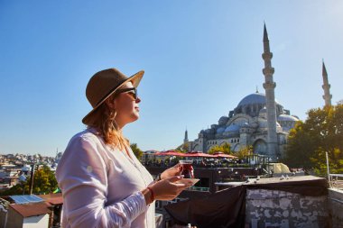 Şapkalı mutlu çekici kadın turist, İstanbul 'daki Süleyman Camii' nin arka planında geleneksel Türk çayı (armuda) içiyor. Din ve seyahat kavramı.