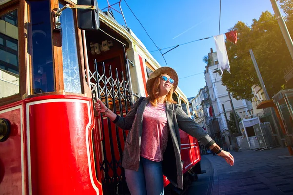 在土耳其伊斯坦布尔碧昂鲁的Istiklal大街上 戴着帽子的漂亮女游客在塔克西姆电车前摆姿势 — 图库照片