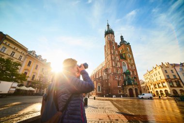 Polonya 'nın Krakow kentinde güneş doğarken ünlü St. Mary Bazilikası' nın fotoğrafını çeken genç ve şık bir kadın turist.
