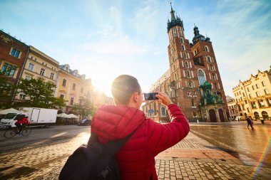 Polonya 'nın Krakow kentinde güneş doğarken ünlü St. Mary Bazilikası' nın fotoğrafını çeken genç bir turist.
