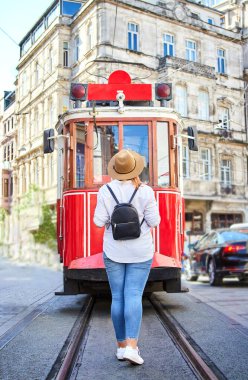 İstanbul, Beyoğlu 'ndaki popüler Istiklal caddesinde, Taksim tramvayı önünde poz veren şapkalı güzel genç kız turist 
