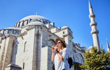 Şapkalı mutlu çekici kadın turist, İstanbul 'daki Süleyman Camii' nin arka planında Simitci (susamlı yuvarlak bir simit) yiyor. Din ve seyahat kavramı.