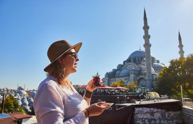 Şapkalı mutlu çekici kadın turist, İstanbul 'daki Süleyman Camii' nin arka planında geleneksel Türk çayı (armuda) içiyor. Din ve seyahat kavramı.
