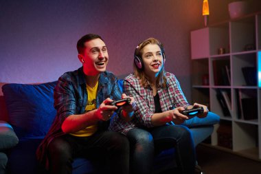 Çılgın, oyuncu bir çiftin portresi, Playstation 'da oyun oynayan oyuncular kanepede oturuyor, konsol Gamepad' i ellerinde tutuyorlar, Xbox hayranları. Evde dinlenmek, iyi hafta sonları.