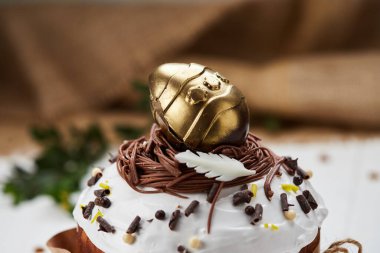 Beyaz ahşap arka planda altın çikolatalı yumurta ile süslenmiş Paskalya pastası geleneksel Kulich, Paska kutlamaya hazır.