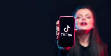 Vinnitsa, Ukrayna - 08 Nisan 2020.Tik tok reklam konsepti. Elinde akıllı bir telefonla poz veren genç bir kız siyah arka planda selfie çekiyor. TIK TOK internette popüler bir sosyal ağ.. 