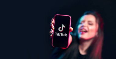 Vinnitsa, Ukrayna - 08 Nisan 2020.Tik tok reklam konsepti. Elinde akıllı bir telefonla poz veren genç bir kız siyah arka planda selfie çekiyor. TIK TOK internette popüler bir sosyal ağ.. 