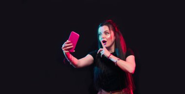 Tik tok reklam kavramı. Elinde akıllı telefonla poz veren, siyah arka planda özçekim yapan genç bir kız. TIK TOK internetteki popüler bir sosyal ağdır.