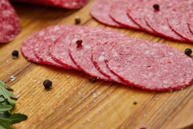 Geleneksel ince dilimlenmiş salam ahşap bir kesme tahtasında baharatlar, marul, avokado ve domateslerle birlikte. Soğuk et tabağı