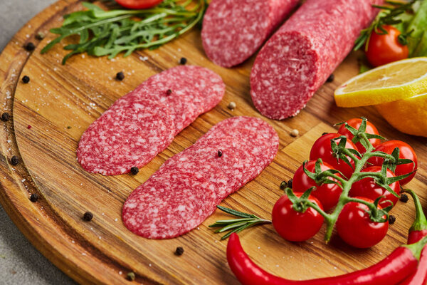 Традиционные тонко нарезанные салями на деревянной доске со специями, салатом, авокадо и помидорами. Холодная тарелка
