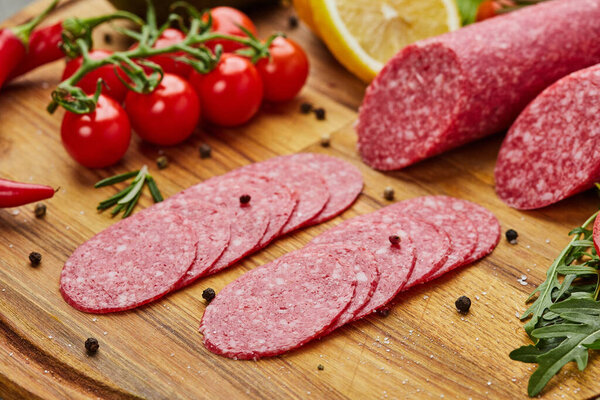 Traditional thinly sliced salami on a wooden cuttingboard  with spices, lettuce, avocado and tomatoes. Cold meat plate