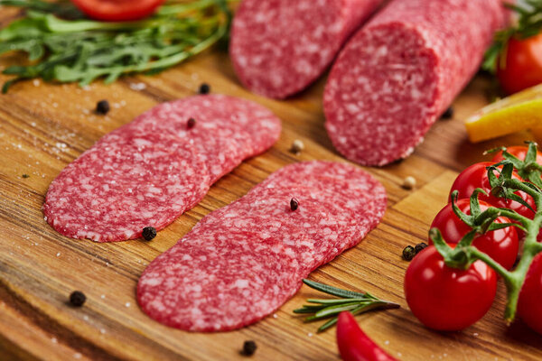 Традиционные тонко нарезанные салями на деревянной доске со специями, салатом, авокадо и помидорами. Холодная тарелка
