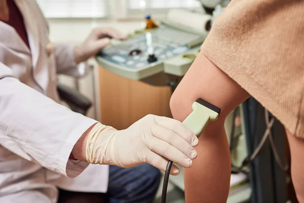 Doctor in white uniform with diagnostic equipment performs an ultrasound examination of leg veins of a female patient. Phlebologist working in modern clinic with Varicose Veins disease